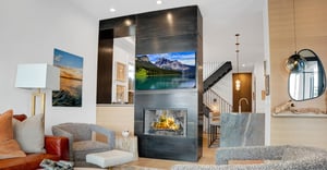 An artistically designed black fireplace mantel with mounted flat screen TV, grey club chair and footrest.