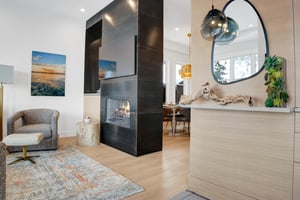 Entryway with mirror, custom ledge, and pendant light, leading to a black fireplace and hardwood floors throughout.