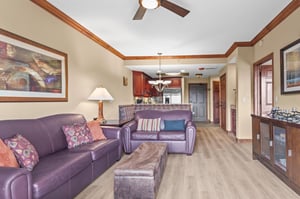 Relax in your spacious living area featuring comfortable purple leather seating, warm wood accents, and an open layout connecting to your fully equipped kitchen.