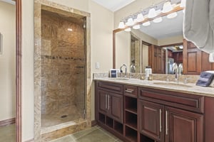 Luxurious master bathroom featuring elegant granite surfaces, rich wood cabinetry, and a spacious stonetiled shower.