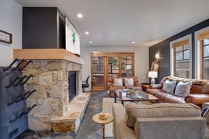 Relax in your spacious living room featuring a stunning stone fireplace, plush leather seating, and warm natural light streaming through large windows.