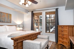 Unwind in your cozy bedroom featuring a comfortable bed, warm wood furnishings, and large windows.