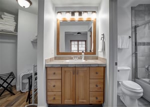 Step into your private bathroom featuring a warm wood vanity with stone countertops, welllit mirror, and separate shower area.