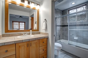 Relax in your private bathroom featuring elegant tile work, a spacious tubshower combo, and warm wood vanity.
