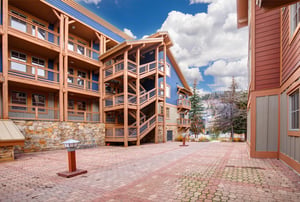 Modern multistory property buildings featuring wood and stone construction with spacious paved courtyard areas for guest access.