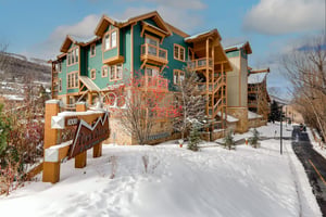 This stunning mountain lodge welcomes you with its charming green facade and warm wood accents, nestled perfectly in fresh powder snow.