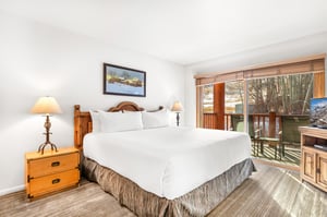 Your comfortable bedroom features a plush bed with crisp white linens, warm wood furnishings, and a private balcony where you can step out and enjoy the natural surroundings.