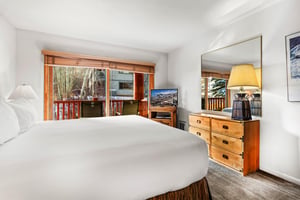 Relax in your comfortable bedroom with warm wood furnishings, a flatscreen TV, and peaceful balcony views of the surrounding natural landscape.