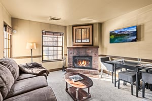 A cozy living room with one sofa, TV, gas burning fireplace, and dining table for two guests.