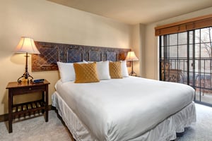 Rest comfortably in your inviting bedroom with plush white linens, warm ambient lighting, and a charming balcony.