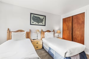 Relax in your comfortable twin bedroom featuring crisp white linens, warm wood furnishings, and bedside lighting.