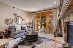 Relax in your stylish living room featuring a cozy stone fireplace, comfortable gray sofa, and warm natural lighting that creates the perfect atmosphere for unwinding.