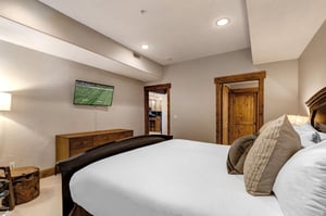 Relax in your spacious bedroom with plush bedding, warm wood accents, and modern amenities including a wallmounted TV for your entertainment.