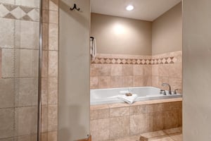 Unwind in your elegant bathroom featuring a soaking tub and separate glass shower, designed with beautiful stone tile accents for your relaxation.
