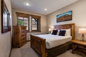 Relax in your cozy bedroom featuring rustic wood furnishings, crisp white linens, and modern amenities including a TV for your evening entertainment.