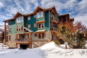 Striking multistory vacation rental building with distinctive green and wood exterior, stone foundation, and mountain lodge architecture.