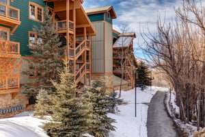 Mountain resort condominiums nestled among snowcovered evergreens, featuring distinctive green and brown architecture with stone accents and wooden balconies.