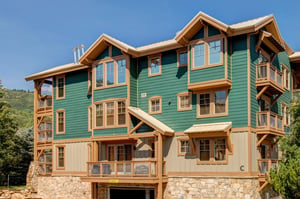 Multistory vacation rental building with distinctive green and natural wood siding, featuring alpinestyle architecture with multiple balconies and large windows.