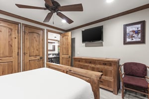 Relax in your cozy bedroom featuring rustic wood furnishings, a wallmounted TV, and charming mountain artwork.