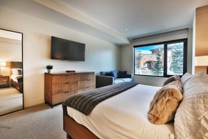 Main bedroom king bed with luxury white linens and cozy throw blanket, wooden dresser with wall mounted flat screen TV