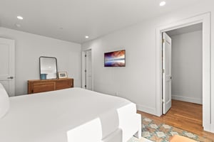 Sink into crisp white linens in your serene bedroom, featuring warm wood floors and thoughtful artwork for peaceful nights.