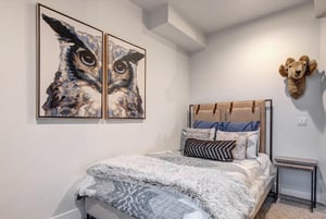 A cozy bedroom with a queensize bed, owl art, and stylish bed frame and linens.