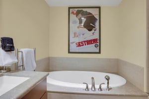 Large soaking tub with tile surround, creamy yellow walls and large picture of a skier above.