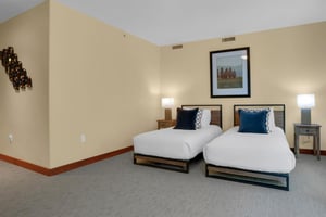 Two twin black and wood framed beds with crisp white linens, two end night stands and lamps, and a one large picture above.
