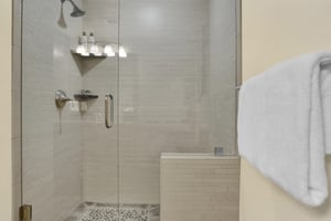 The walk in shower has cream colored tile walls, stone floor and a glass enclosure door.