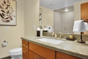 Bathroom with toilet, one sink wooden vanity, large mirror, and creamy yellow walls.