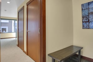 The entryway with a bench, and a hall with two doors, cream colored carpet and creamy yellow colored walls.