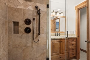 The shared bathroom has a walkin shower with a glass door and beautiful tile.