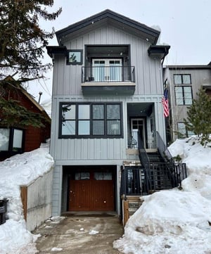 Classic Historic District row home exterior with grey siding, warm wooden garage door and black windows and trim.