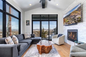 The living room has a plush sectional, gas burning fireplace, and large windows framing mountain views.ceiling windows.