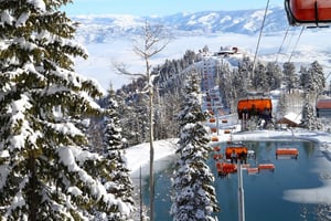 The Canyons ski area orange bubble lift traveling over a snowy mountain with icy lake below.
