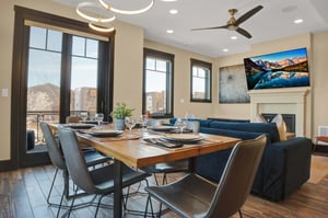 Wood dining table with 6 leather chairs and a large window behind the table.