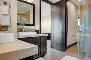 The en suite bathroom has two sinks with a dark wood vanity and doors and light warm walls.