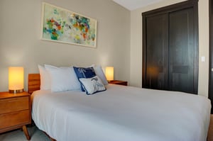The second bedroom with a queen size bed with crisp white linens and a colorful piece of modern art hanging above.