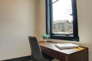 An office nook with wooden desk with grey leather chair in front of a window.