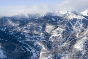Aerial view of Canyons Resort with snow covered mountains, ski runs, and trees.