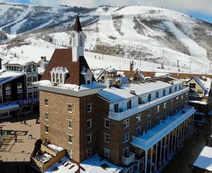 Ariel view of Resort Plazas large brick building with Park City Mountain ski runs covered in snow directly behind.