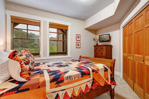 Settle into your cozy bedroom with rich wood tones, a vibrant quilt, and windows framing natural hillside views. Your dresser holds a flatscreen TV, and your wardrobe offers ample closet space for un