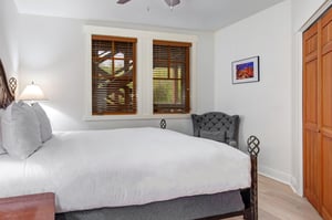 Slip into crisp white linens and unwind in your serene bedroom retreat. Natural light filters through wooden blinds, a plush reading chair invites relaxation, and ceiling fan comfort awaits.