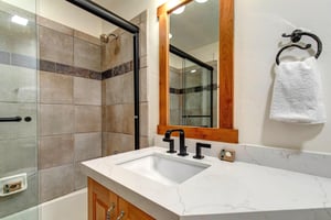 The shared bathroom with a warm wood single sink vanity and a bathtub and shower combination.
