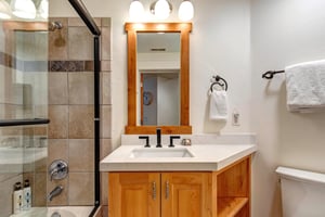 The shared bathroom with a warm wood single sink vanity and a bathtub and shower combination.
