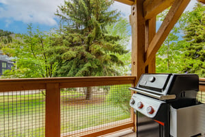 Your private balcony awaits with a sleek gas grill ready for outdoor cooking, framed by lush evergreens and open mountain views that invite you to unwind.
