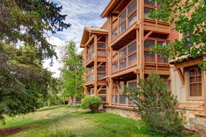 A multistory timberframe building nestled among evergreens and deciduous trees, featuring extensive screened balconies and natural stonework at the base, photographed during daytime.