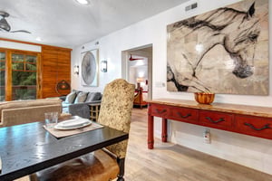 The dining room has large art on the wall over a side board and plush dining room chairs.
