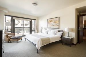 Main bedroom with king bed, bedside tables, comfortable lounge chair with leather foot stool