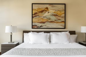 Luxurious king bed in the main suite, white linen and duvet cover with mountain modern art above the wooden headboard